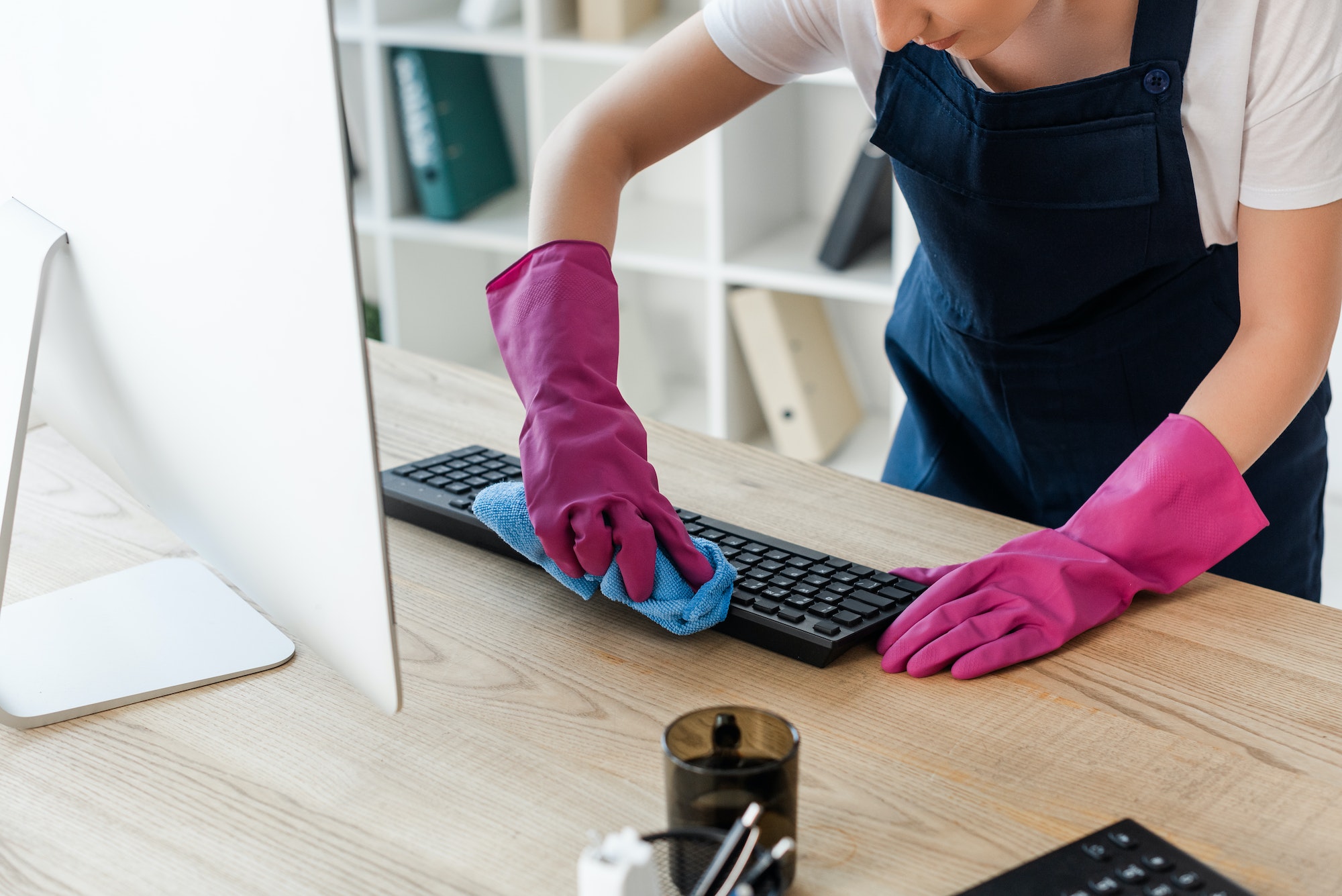 Cropped view of cleaner in rubber gloves cleaning computer keyboard in office